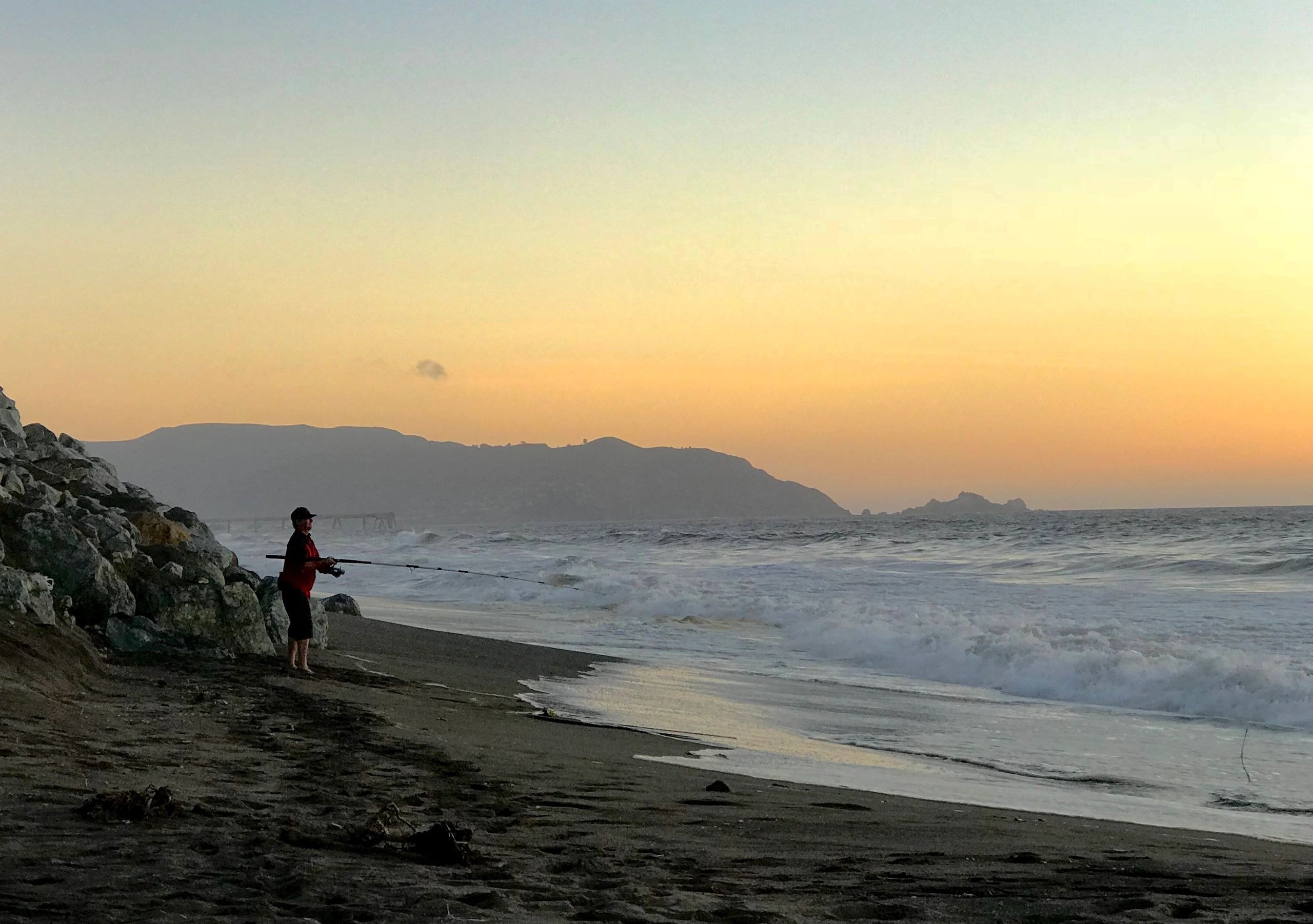 Person fishing on beach at sunset